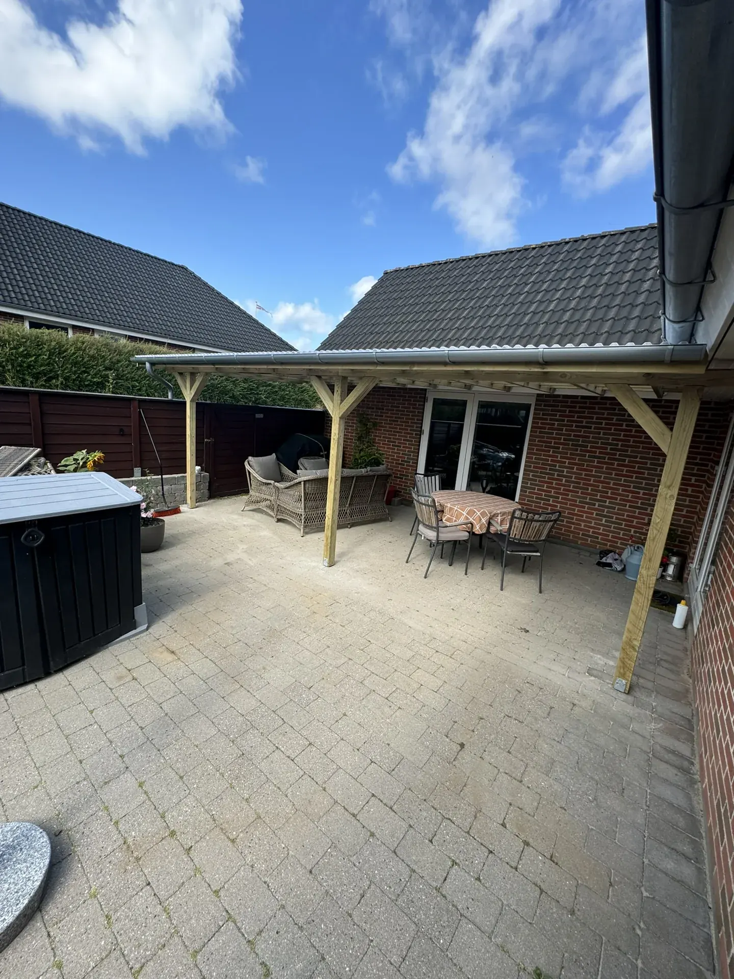 Overdækket terrasse med træspær ved rødt murstenshus
