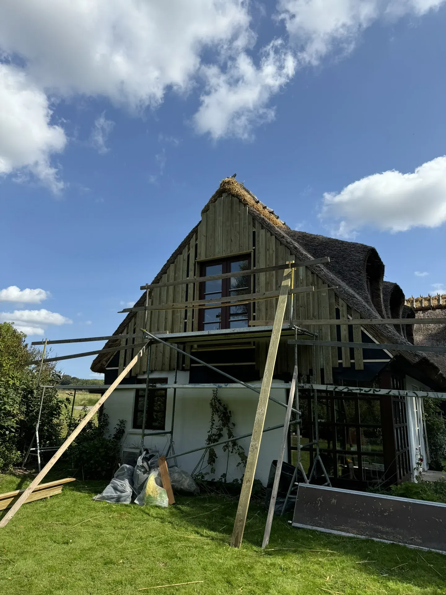 Stråtækt hus med stillads, hvor en ny trægavl bygges op