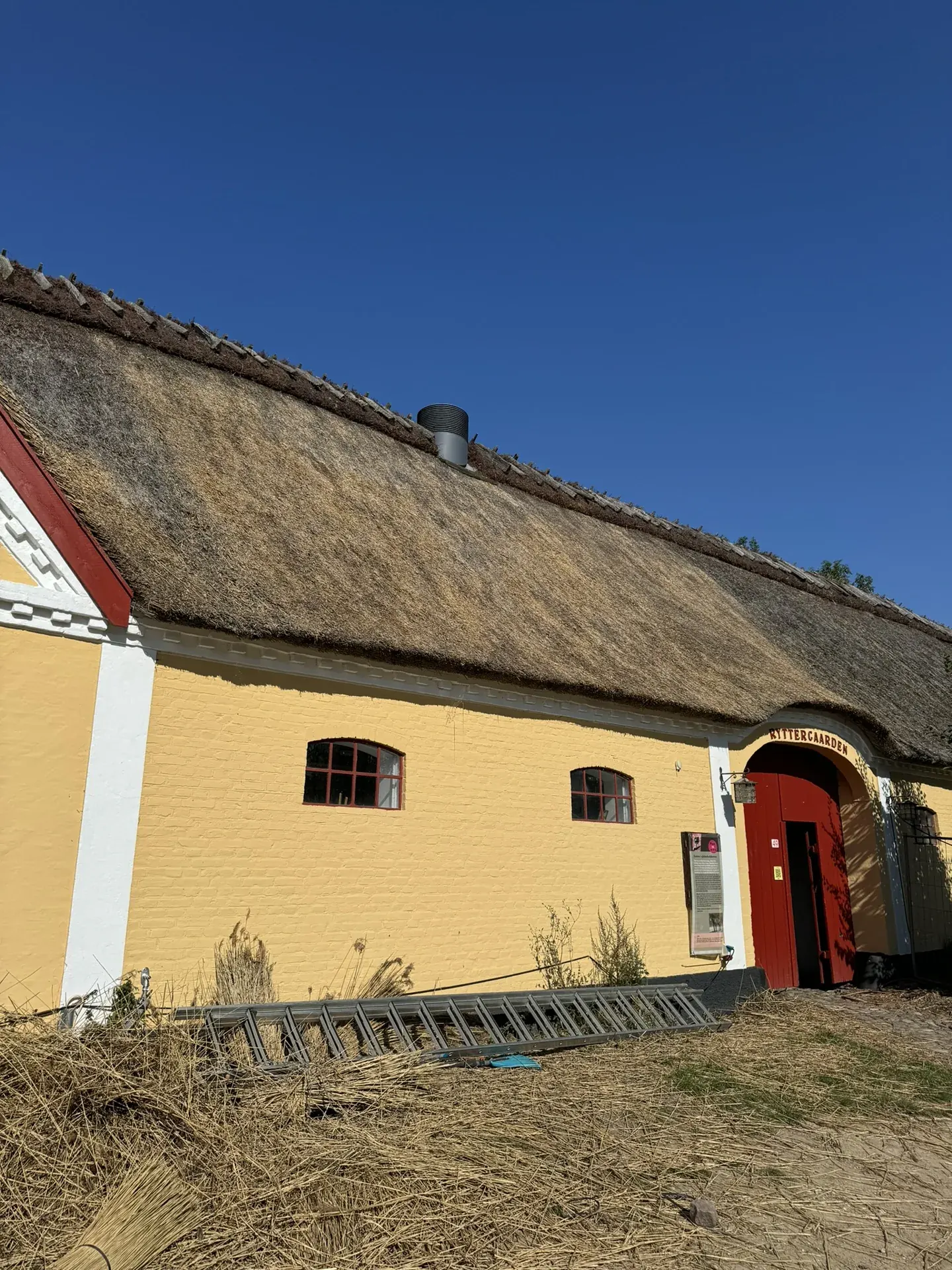 Langt stråtækt hus med gul facade under tagarbejde