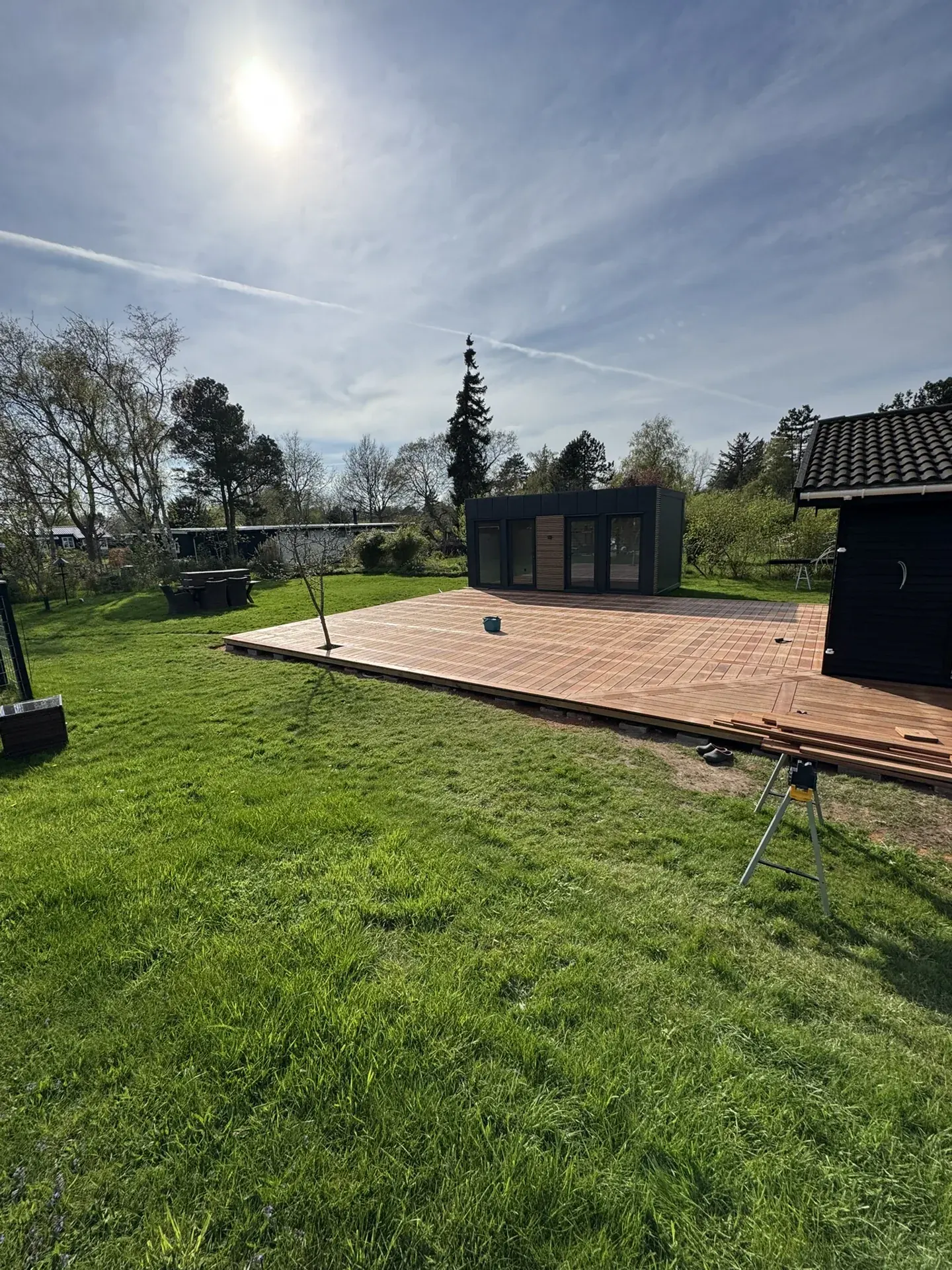 Færdig terrasse ved sort sommerhus set fra haven