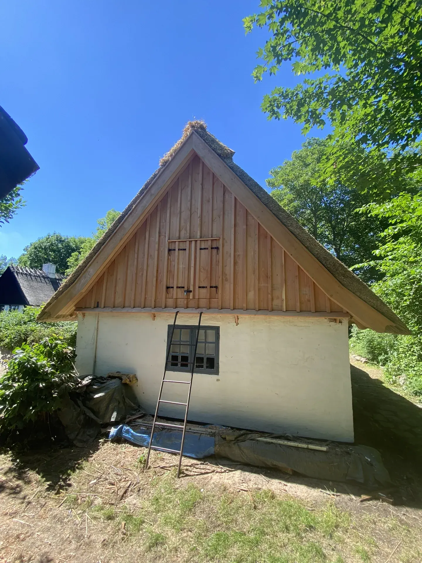 Færdig gavl med lodret træbeklædning på hvidkalket hus med stråtag